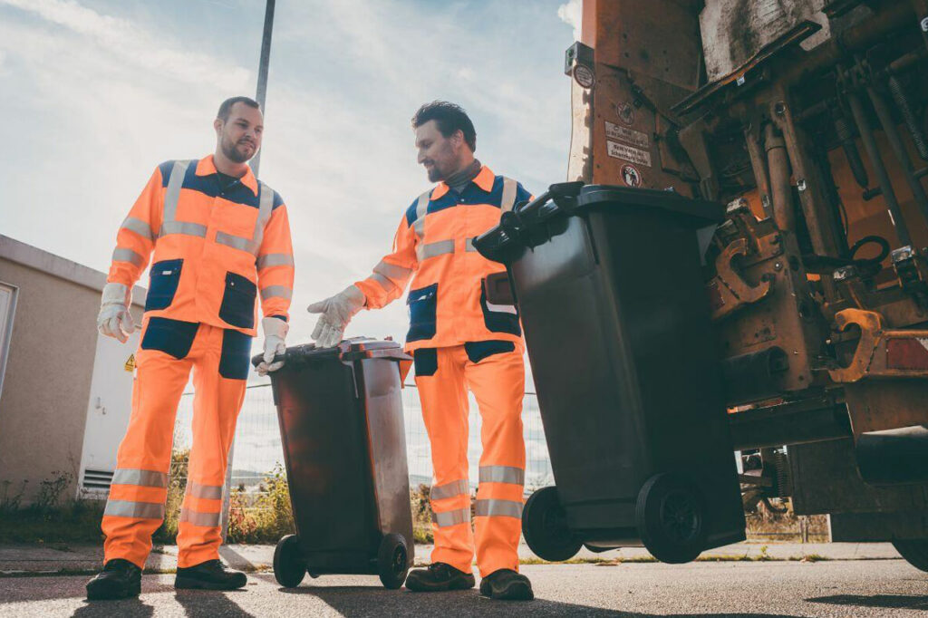 Two men in orange uniforms working in waste management industry