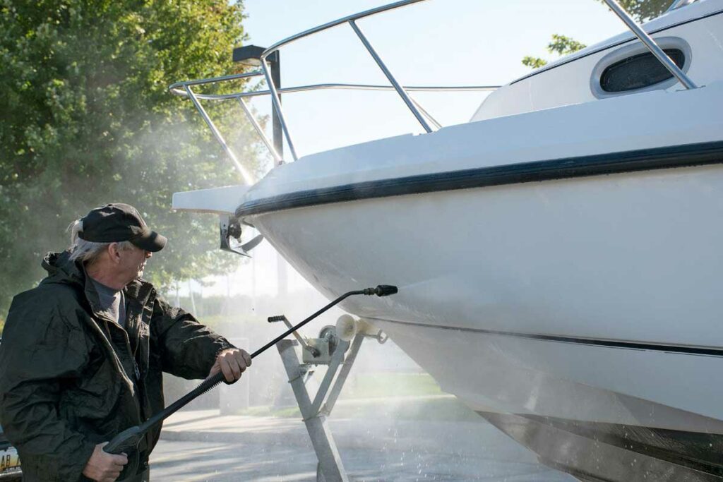 man cleaning a sailboat with a pressure washer