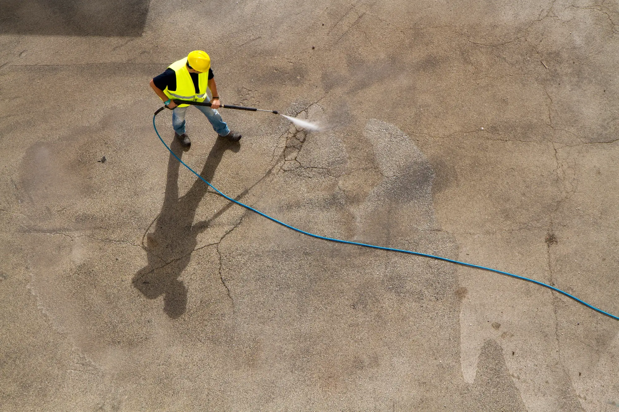 Man wearing construction equipment pressure-washing concrete