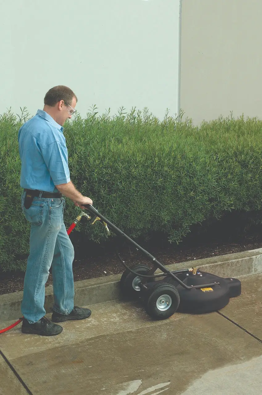 Man using a water broom to clean concrete