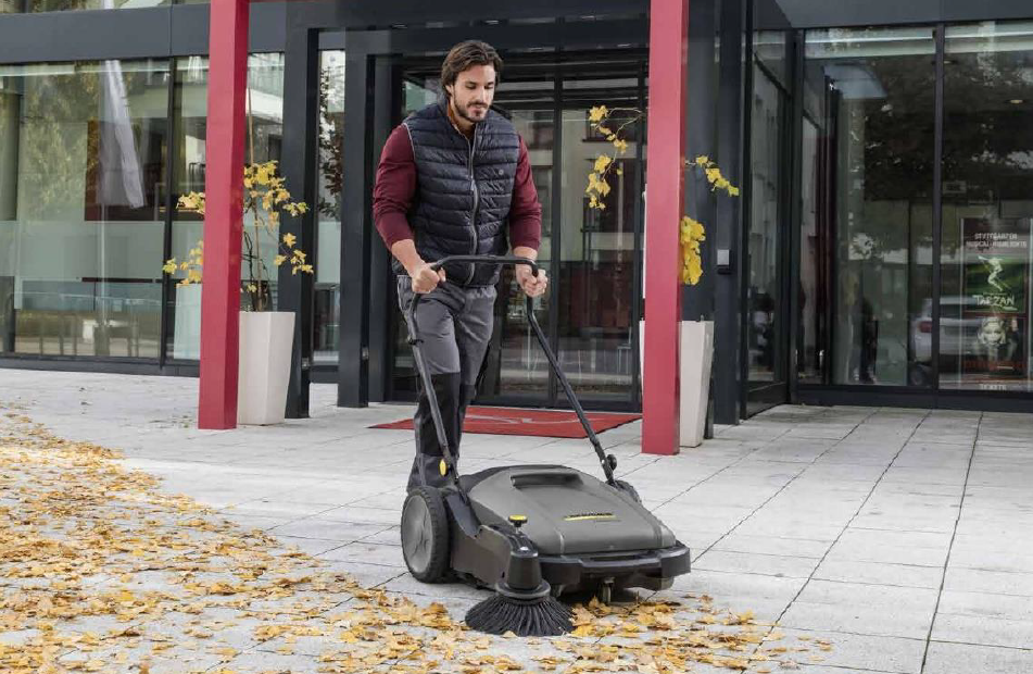 A man uses a floor sweeper to clean a commercial building entrance floor. 