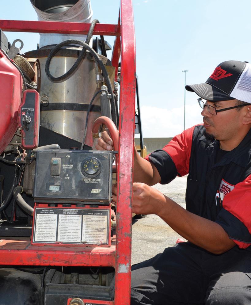 Hotsy technician adjusting temperature settings on a red industrial pressure washer unit outdoors
