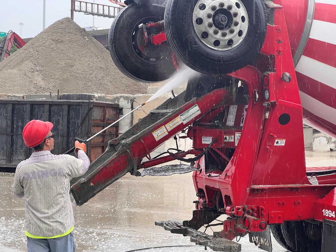 Worker using pressure washer to clean cement mixer at job site