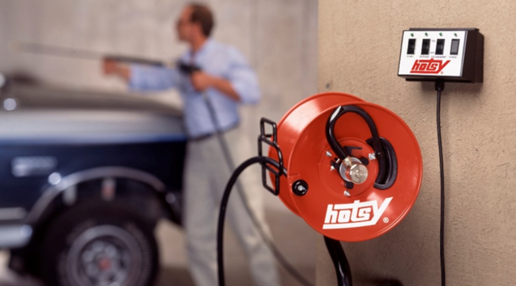 Hotsy hose reel and man pressure washing a vehicle in background