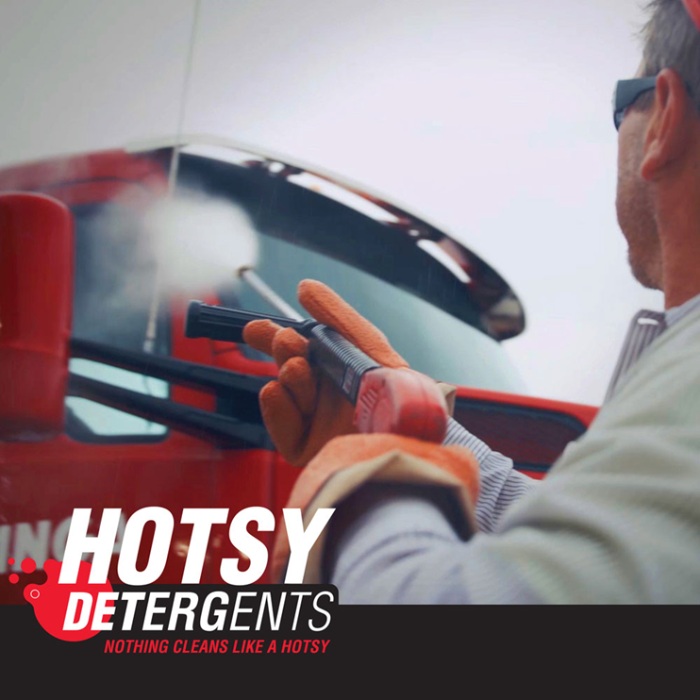 Man using Hotsy pressure washer on red truck with detergent branding