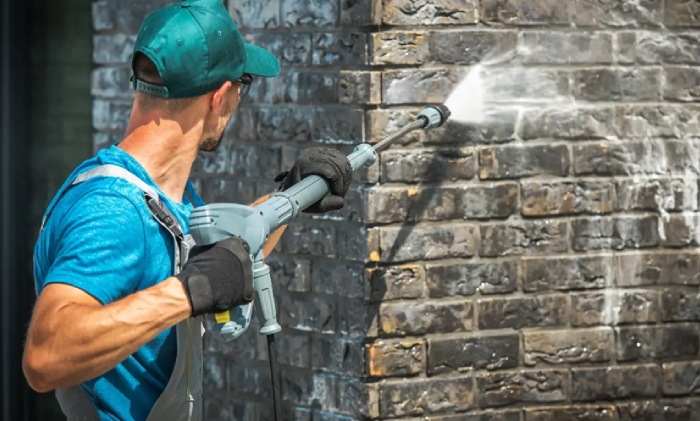 Worker pressure washing a brick wall with a high-pressure washer to remove dirt and grime