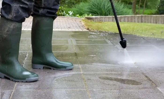 Worker using a pressure washer to clean concrete pavement outdoors
