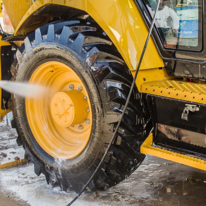 Close-up of a heavy equipment truck being pressure washed, with water spraying onto the tire.